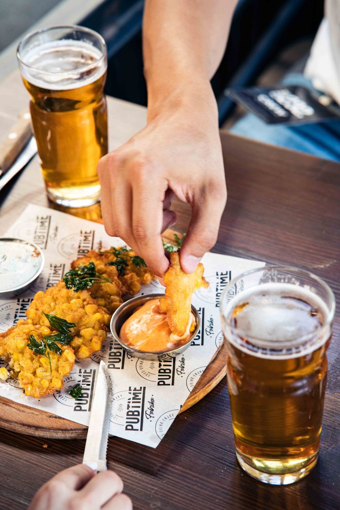 Hand dipping fried appetizer into sauce accompanied by beers in a pub setting.