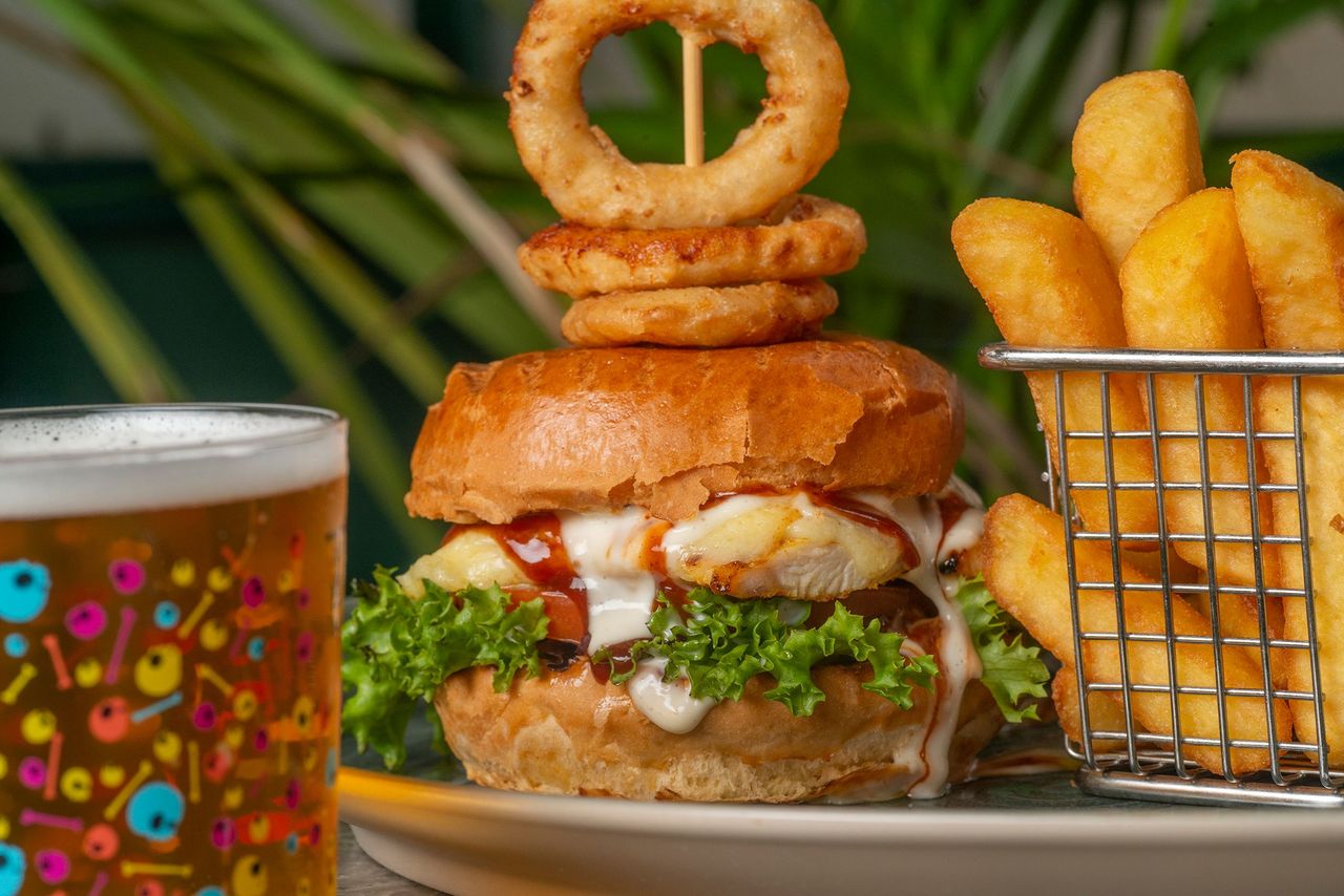 Tasty burger topped with onion rings, served with a side of fries and a refreshing drink.