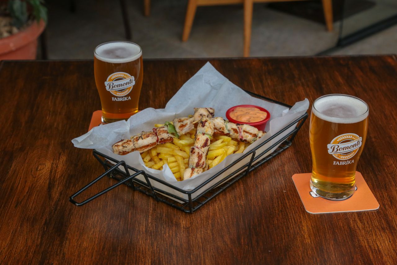 A casual dining setup with beer, grilled skewers, and fries served indoors.