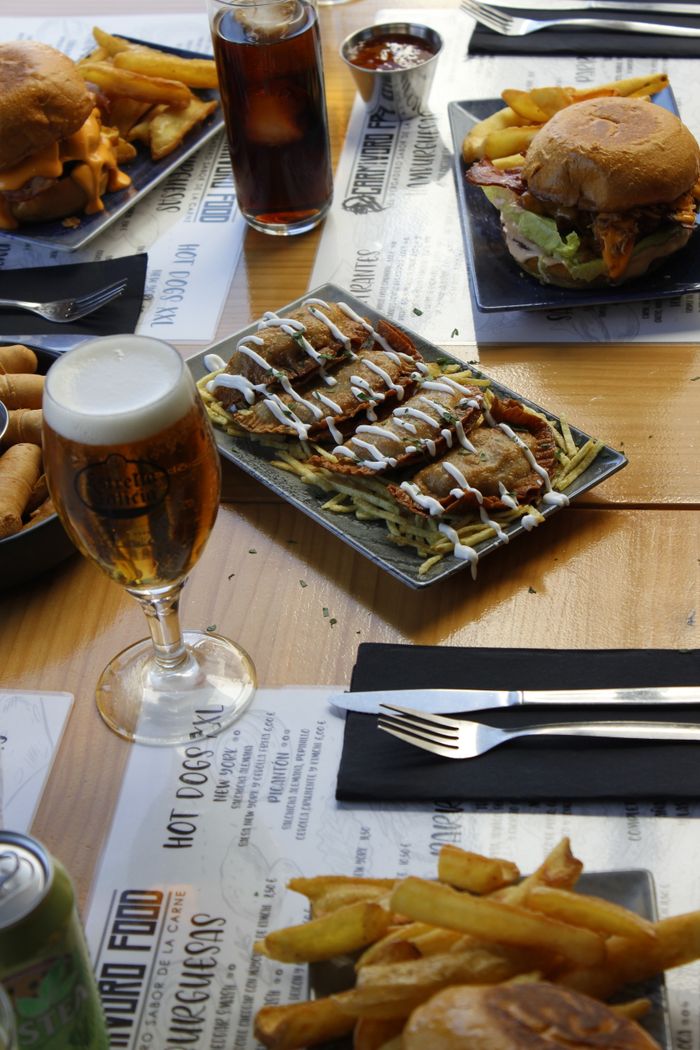 A tempting spread of fast food including burgers, tacos, beer, and fries on a wooden table.