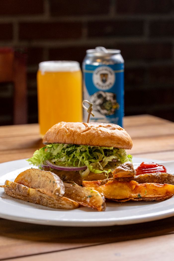 Mouthwatering burger served with fries and craft beer on a wooden table in a cozy setting.