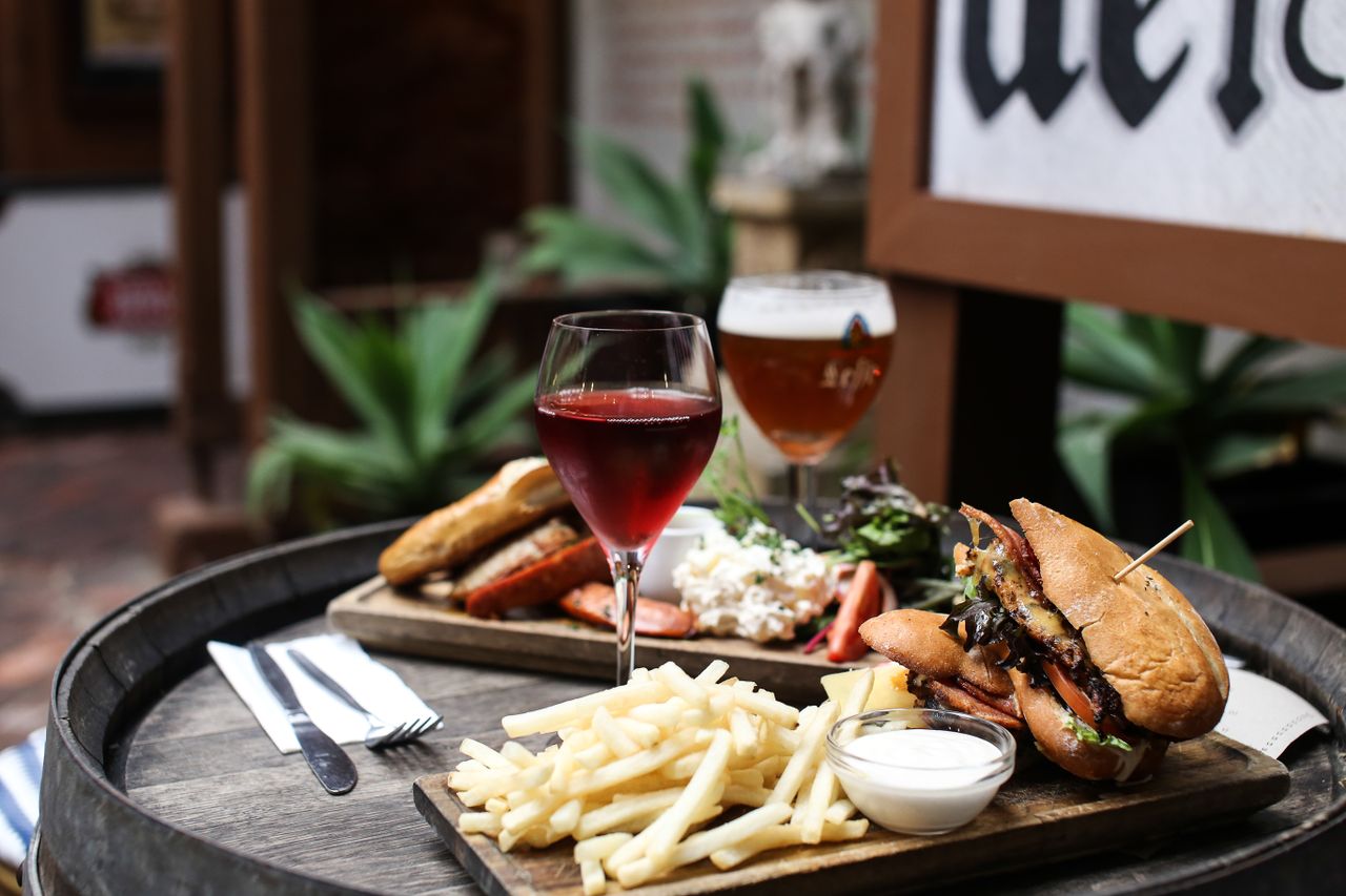Enjoy a delicious gourmet burger meal with fries and wine in a cozy, rustic restaurant ambiance.