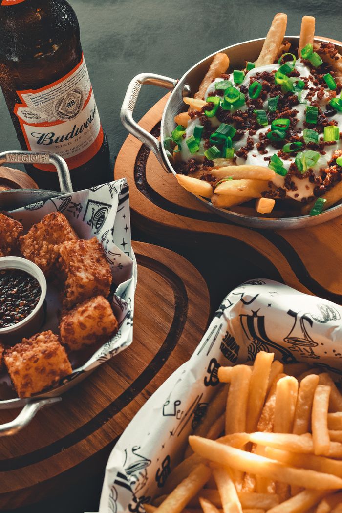 A close-up of a savory bar meal featuring varied fries and a beer bottle on a wooden table.